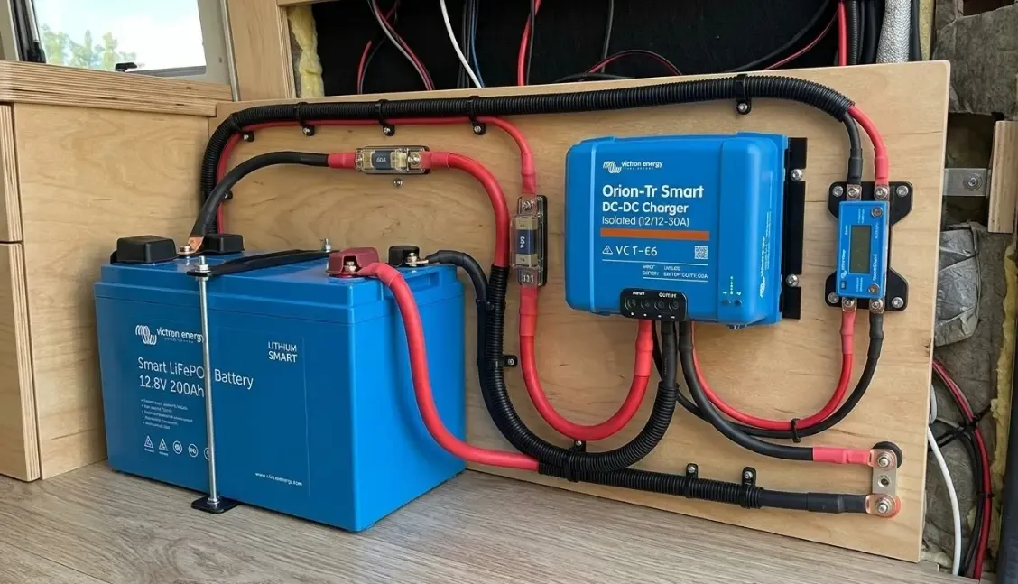 Instalación profesional de un cargador DC-DC azul de la marca Victron Energy en una furgoneta camper, conectado con cables gruesos a una batería de litio